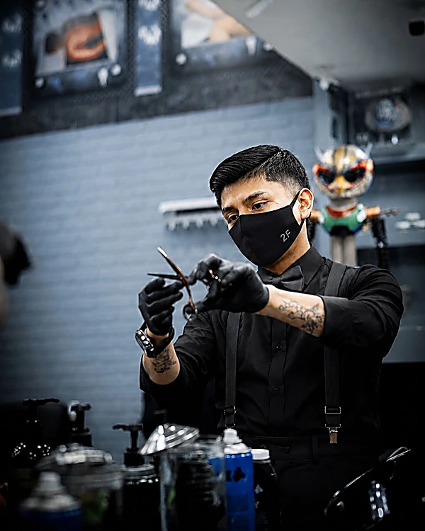 Barbero de 2F con cubrebocas y guantes negros preparando sus tijeras en su estación