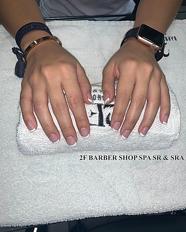 Manos con manicure en tono nude apoyadas sobre una toalla blanca con la leyenda 2F Barber Shop Spa Sr & Sra