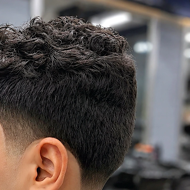 Cabello rizado con textura arriba y degradado limpio en el costado, visto desde la oreja